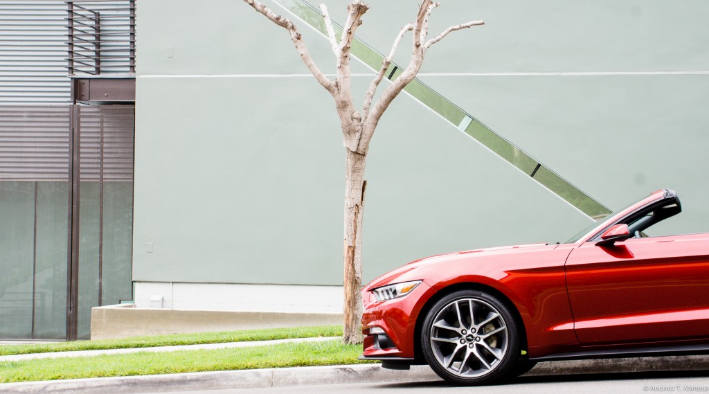 Front end of a red 2015 Mustang convertible parked in front of a tree.