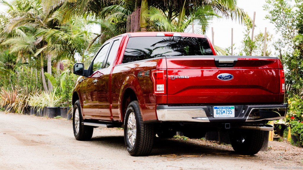 A Cherry Red Ford F150 pickup truck parked in front of some palm trees.